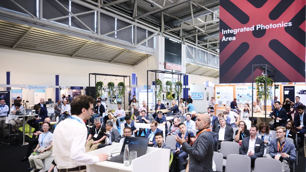 Vortrag auf der Messe Laser World of Photonics vor Publikum, im Hintergrund Messestände und ein Schild „Integrated Photonics Area“