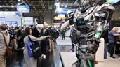 Überlebensgroßer Roboter im Transformer-Look gibt einer Besucherin auf der Messe die Hand.