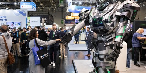 Überlebensgroßer Roboter im Transformer-Look gibt einer Besucherin auf der Messe die Hand.