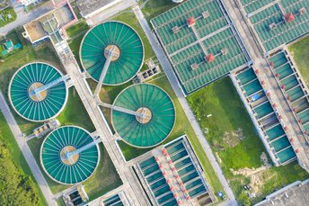 Innovative Wasseraufbereitung im EinsatzLuftaufnahme einer modernen Kläranlage mit großen runden Becken und rechteckigen Filteranlagen zur Wasseraufbereitung.