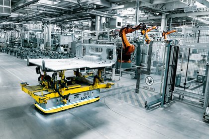 A robotic arm is working in a state-of-the-art, automated production line on a car sheet that is being moved on an automated pallet.
