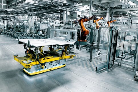 Ein Roboterarm arbeitet in einer hochmodernen, automatisierten Fertigungsanlage an einem Autoblech das auf einer automatisierten Palette bewegt wird.