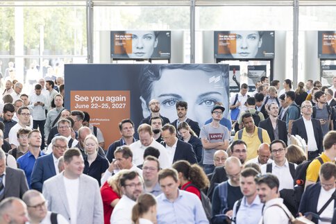 A large crowd of trade fair visitors moves through the bright entrance hall of Messe München. At the center, a large sign reads “See you again – June 22–25, 2027”