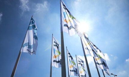 Flags with the Messe München and IFAT Munich logos fly on poles against a sunny blue sky.