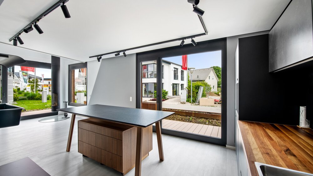 Moderne Küche mit elegantem schwarzen Esstisch, Holztheken, großen Fenstern und Blick auf die Häuser draußen.