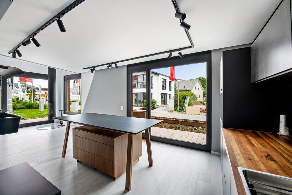 Moderne Küche mit elegantem schwarzen Esstisch, Holztheken, großen Fenstern und Blick auf die Häuser draußen.