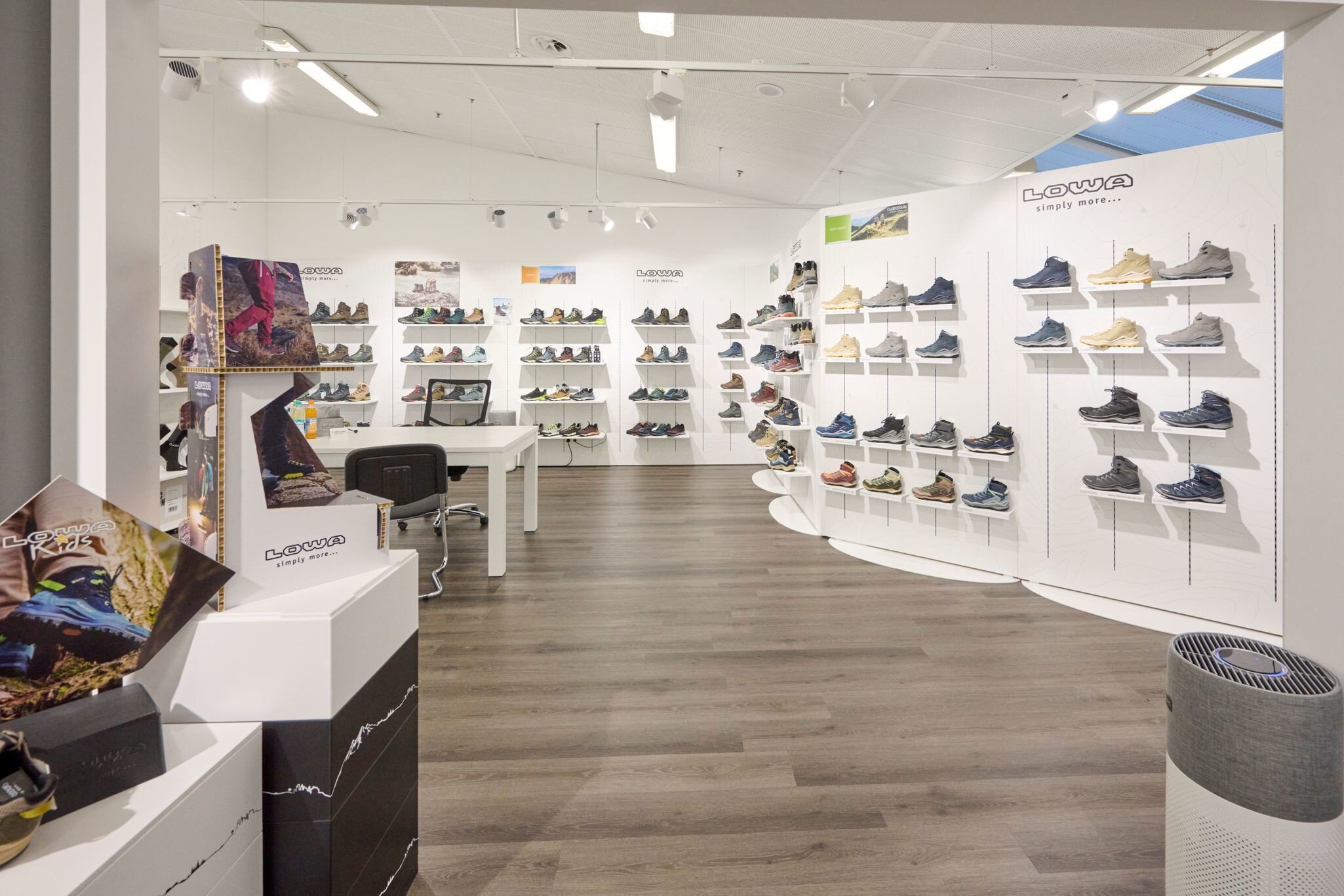 Modernes Schuhgeschäft mit weißen Wänden, Holzfußboden und Regalen, in denen verschiedene Sportschuhe ausgestellt sind.