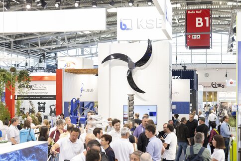 Blick in Halle B1 der Messe München mit zahlreichen Messebesuchern, die zwischen unterschiedlichen Messeständen stehen. An einer Stellwand hängt ein schwarzer Propeller.