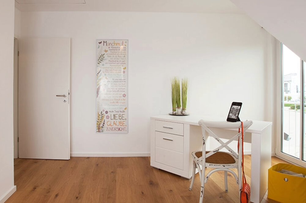 Minimalistischer Raum mit weißen Wänden, einem kleinen Tisch mit Stuhl, einer grünen Pflanze, Wandkunst und einem Fenster mit Sonnenlicht.