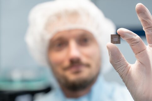 Person im Reinraum hält einen Mikrochip zwischen den Fingern.
