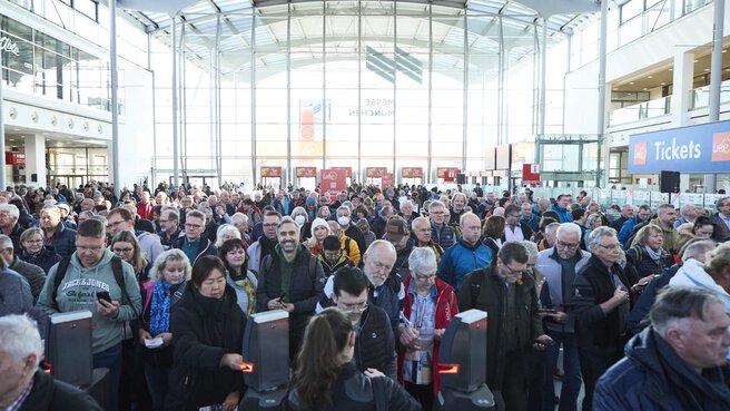 Blick in die Eingangshalle einer Messe, wo viele Besucher an den Drehkreuzen anstehen.