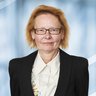 A woman with short red hair, glasses and a suit jacket with a light-colored blouse.