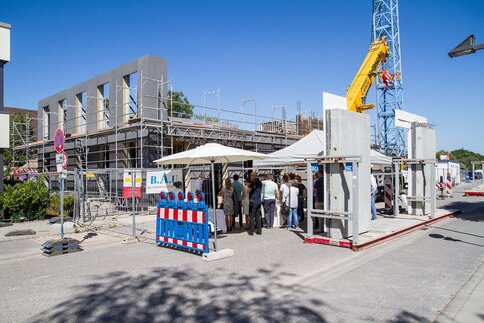 Construction site with a multi-storey building under development and a group of people under umbrellas.
