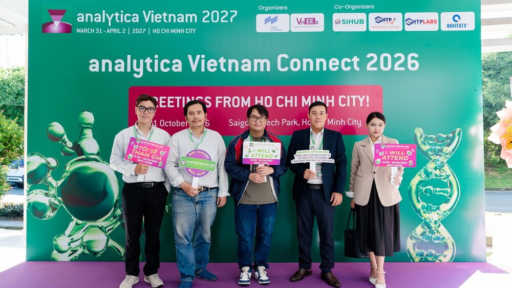 Fünf Personen stehen vor einem Banner der analytica Vietnam 2027 in Ho-Chi-Minh-Stadt und halten Schilder mit Veranstaltungsbotschaften in den Händen.