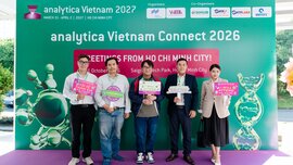 Fünf Personen stehen vor einem Banner der analytica Vietnam 2027 in Ho-Chi-Minh-Stadt und halten Schilder mit Veranstaltungsbotschaften in den Händen.