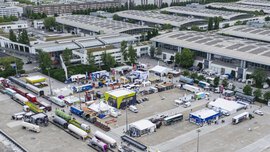 Vogelperspektive auf das Freigelände der Messe München während der transport logistic mit Ausstellerständen und Eisenbahnwagons daneben.
