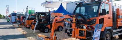 Open-air exhibition of construction machinery with orange equipment and blue tents.