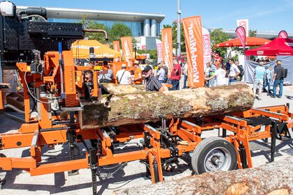Mobile sawmill processing logs at an outdoor trade fair while visitors explore the machinery.