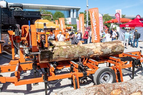 Mobile sawmill processing logs at an outdoor trade fair while visitors explore the machinery.