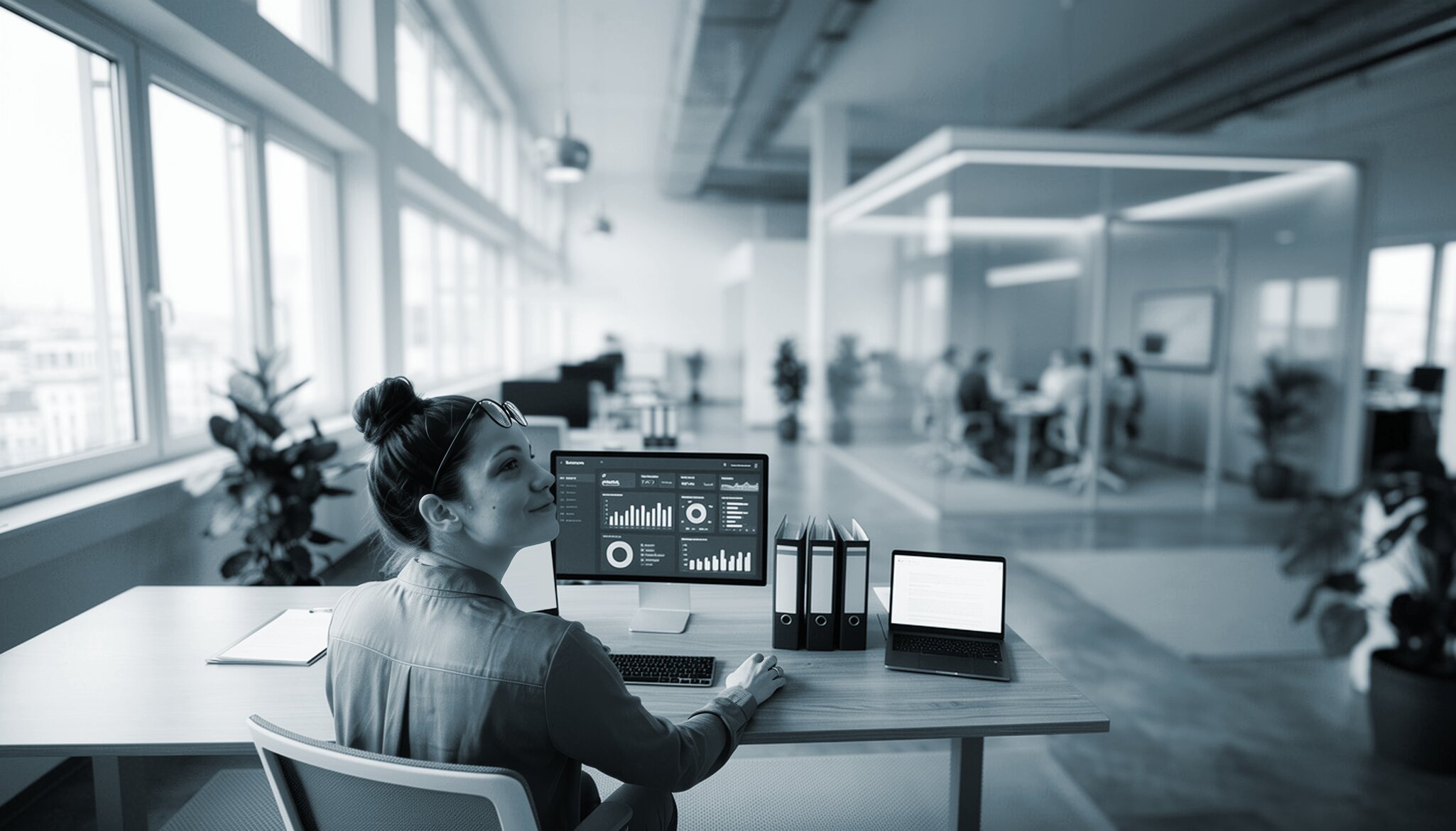 Woman sitting at a desk in front of a screen displaying charts.