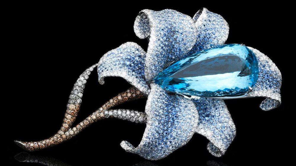 Close-up of a blue elongated gemstone in the center of a blue decorative flower with a brownish stem.
