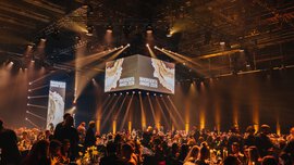 A banquet hall with numerous bright orange spotlights illuminating a large audience seated at numerous tables.