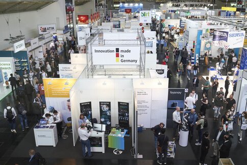Vogelperspektive auf eine volle Messehalle. Im Mittelpunkt ist ein deutscher Gemeinschaftsstand