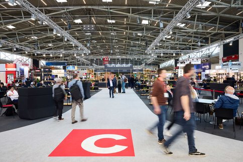 A central exhibition hall with a catering and networking area where visitors move, meet, and interact.