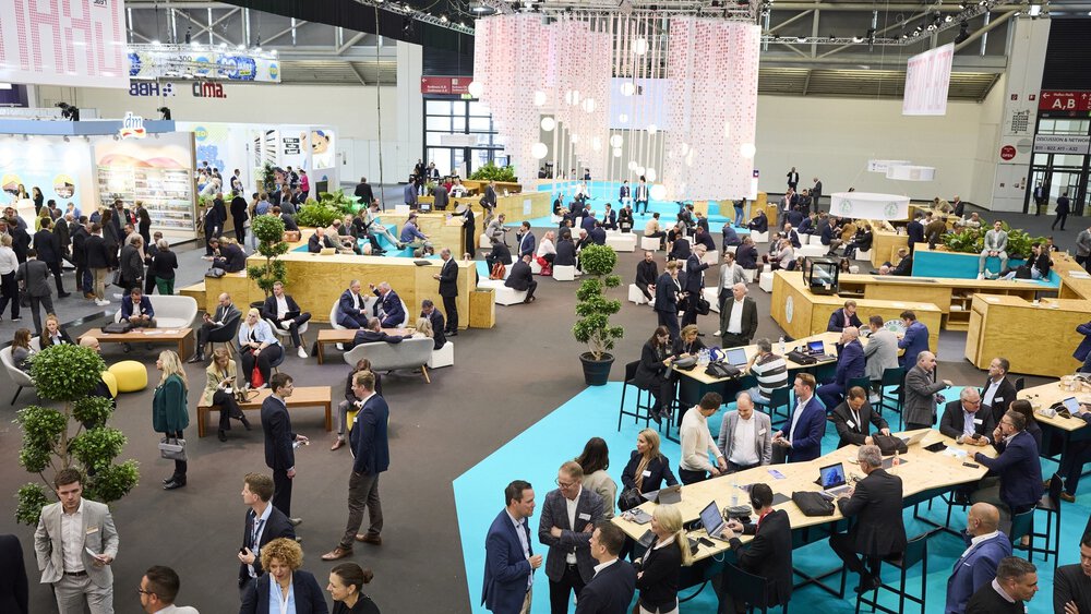 In einem weitläufigen Arbeits- und Meetingbereich der EXPO REAL arbeiten und unterhalten sich zahlreiche Messebesucher.