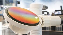 Nahaufnahme eines weißen zylindrischen technischen Gerätes auf dem eine bunt schillernde, irisierende Scheibe montiert ist.
