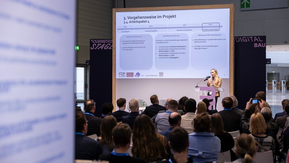 Eine Frau präsentiert dem Publikum einer Konferenz in einer modernen Halle eine Projektfolie.