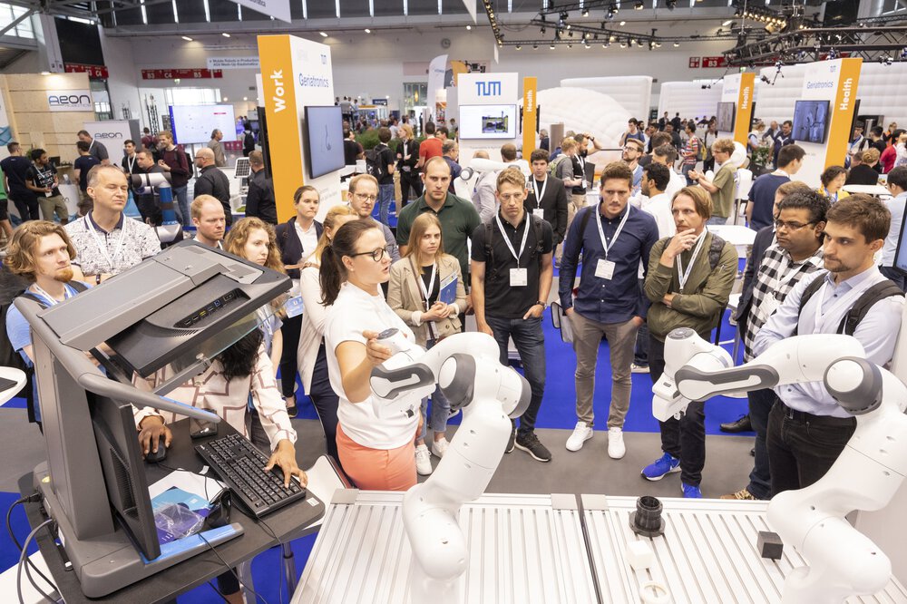 A woman presents the functions of two modern robot arms to an interested audience at the automatica exhibition.