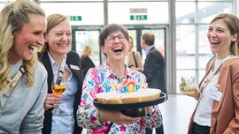 Four women laughing together at the trade fair; one holds a birthday cake with 