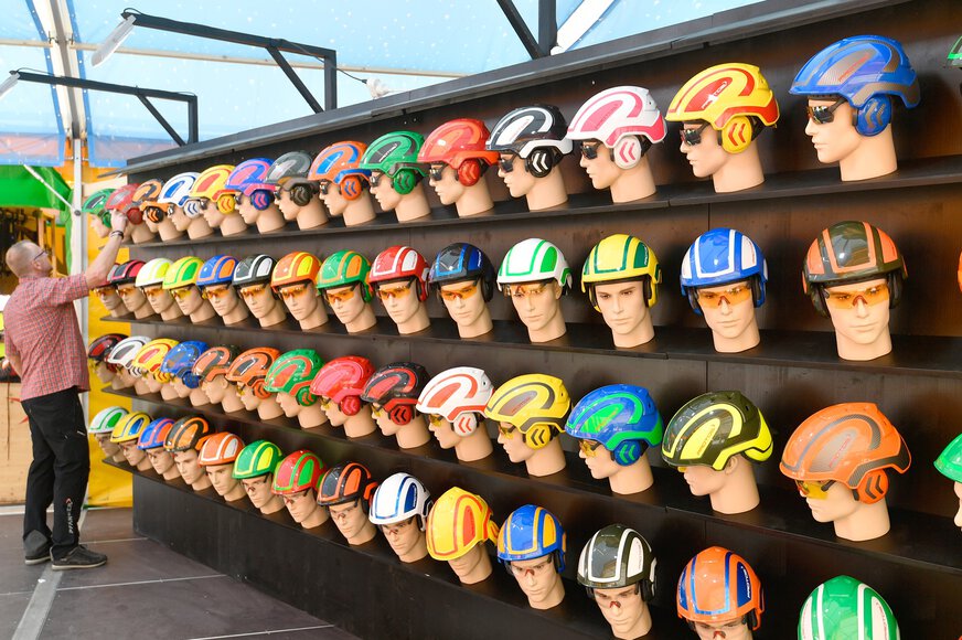 A wall of shelves full of mannequin heads with safety goggles and bright safety helmets in a wide variety of colours.