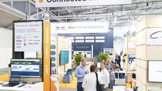 Messestand mit dem Schild „Connected Machines“ in einer hellen Messehalle. Im Vordergrund ist ein Informationsbereich mit Monitoren und Logos namhafter Unternehmen wie Atlas Copco und Bosch Rexroth zu sehen. Im Hintergrund präsentiert Mech-Mind Robotics KI-gestützte Automatisierungslösungen. Messebesucher unterhalten sich angeregt.