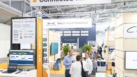 Messestand mit dem Schild „Connected Machines“ in einer hellen Messehalle. Im Vordergrund ist ein Informationsbereich mit Monitoren und Logos namhafter Unternehmen wie Atlas Copco und Bosch Rexroth zu sehen. Im Hintergrund präsentiert Mech-Mind Robotics KI-gestützte Automatisierungslösungen. Messebesucher unterhalten sich angeregt.