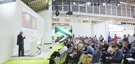 Ein Redner präsentiert auf der Bühne des Laser Materials Processing Photonics Forum in einer Messehalle.