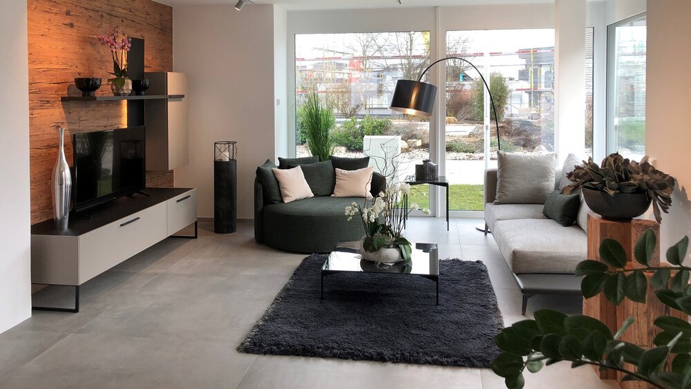 Zeitgenössisches Wohnzimmer mit großen Fenstern, modernem Sofa, Fernseher an einer Holzwand und einem Couchtisch aus Glas.