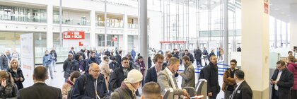 People walk through the ticket barriers in a busy, modern atrium with glass walls and ceilings.