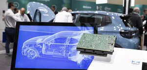 A display with the grid model of a car is shown on a pedestal, with a circuit board in front of it. A real car and visitors can be seen out of focus in the background.