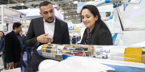 Two people look smilingly at the model of an airplane with a transparent cargo hold in which various goods are displayed.