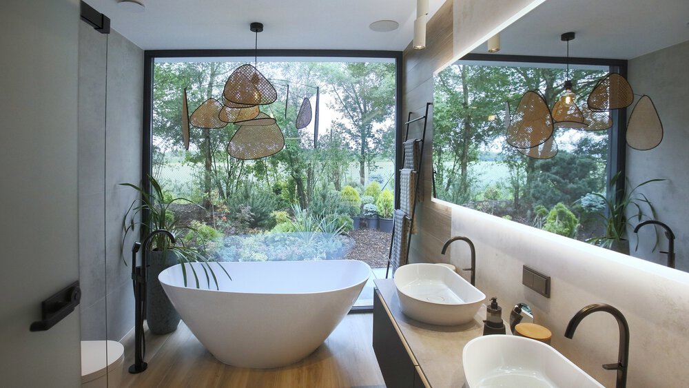 Modernes Badezimmer mit freistehender Badewanne, großem Fenster mit Blick ins Grüne, Doppelwaschbecken und zeitgenössischer Einrichtung.