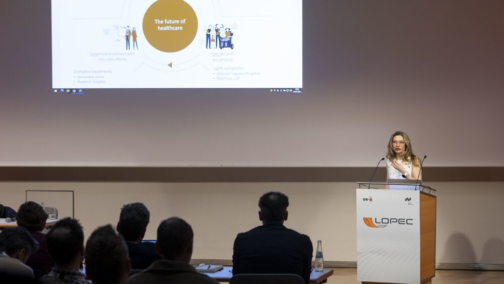 Eine Frau an einem Podium auf der LOPEC hält einen Vortrag vor einem Publikum. Im Hintergrund ist eine Präsentationsfolie zum Thema „The future of healthcare“ zu sehen.