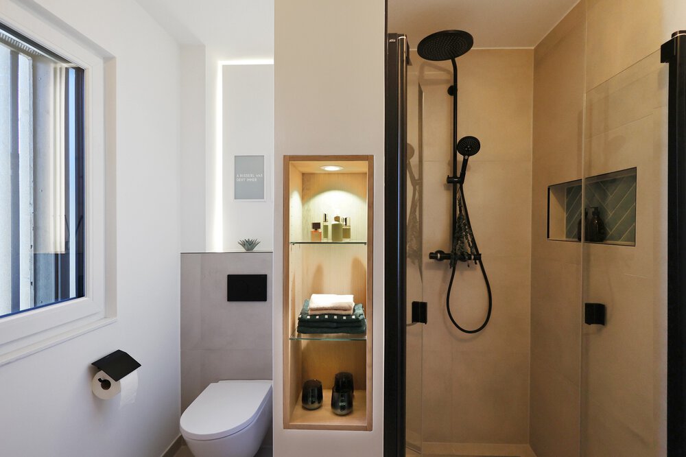 Modernes Badezimmer mit Glasdusche, Wand-WC, beleuchtetem Regal und einem Fenster mit Tageslicht.