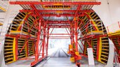Large tunnelling machine with metal scaffolding, red and yellow frame and exposed railway tracks.