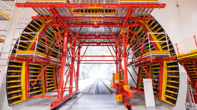 Large tunnelling machine with metal scaffolding, red and yellow frame and exposed railway tracks.