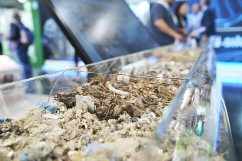 Nahansicht eines länglichen, oben offenen Behälters, in dem feinteilige Abfallprodukte in unterschiedlicher Zusammensetzung ausgestellt sind.