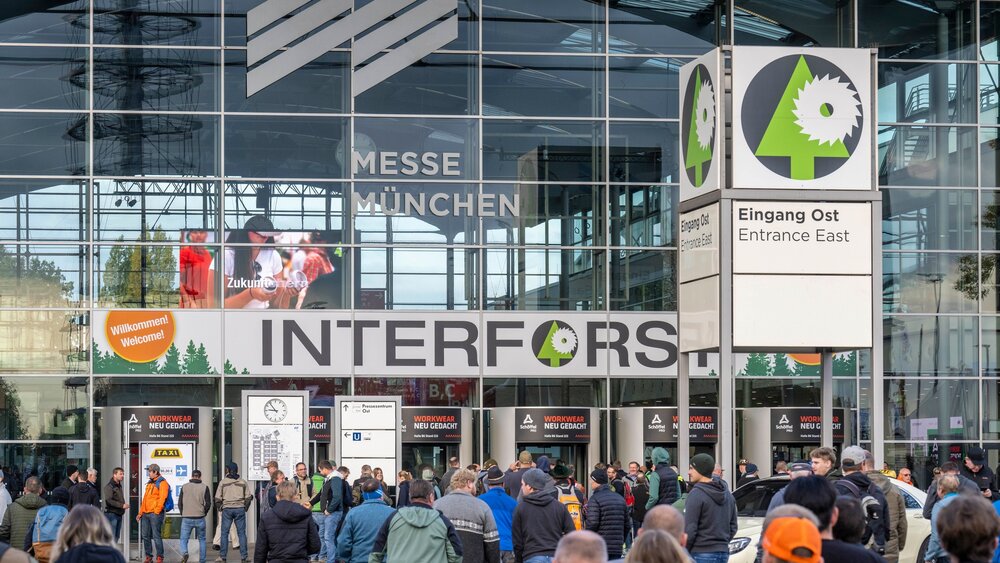 Numerous visitors in front of the east entrance of Messe München with a large INTERFORST sign.