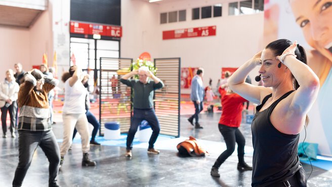 Eine Gruppe von Menschen macht Yoga Übungen in einer Messehalle