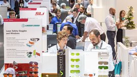 People at an exhibition stand displaying various laser safety goggles and glasses.